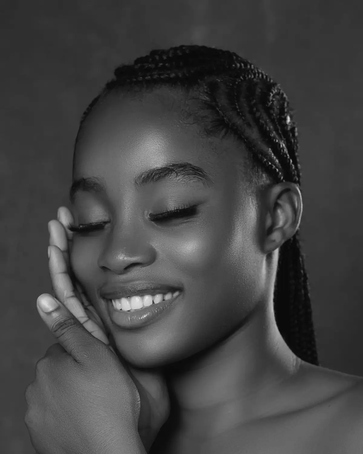 A smiling woman with eyes closed, hand resting on her cheek