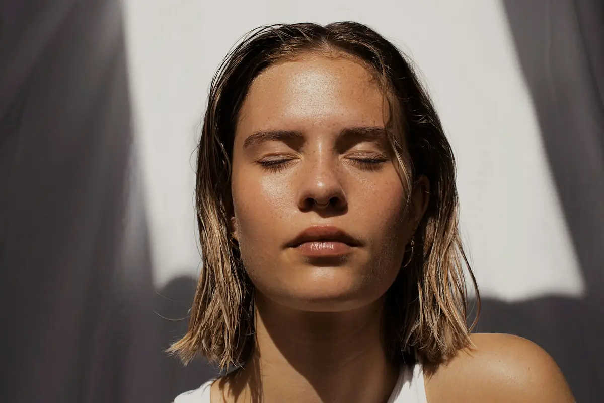 A woman with eyes closed in soft window light, skin calm and even